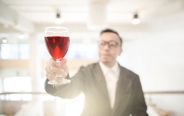 Happy Asian rich man smiling while holding a glass of red wine in the party hall