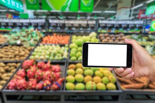 Hand holding smartphone with white blank screen and blurred supermarket fruit background
