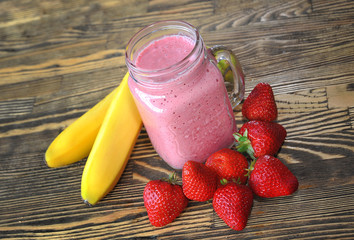 Fruity strawberry smoothies with a banana on a wooden table.