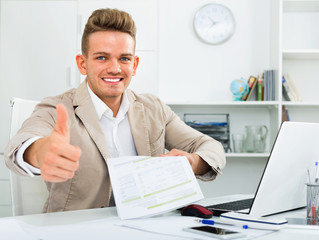 Portrait of businessman showing thumbs up in modern office