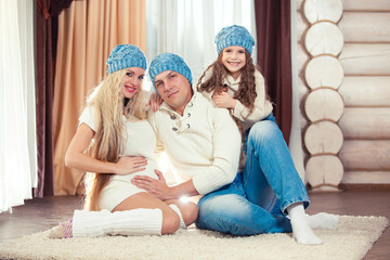 Young family sitting on floor. in a winter sweater and hat, the concept of Christmas. pregnancy in a wooden house