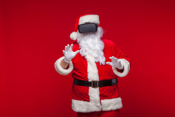 Santa Claus wearing virtual reality goggles, on a red background. Christmas