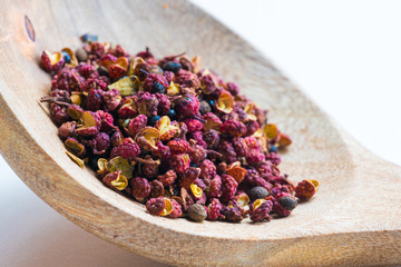 Sichuan red peppercorn close-up in a wood spoon on a white table