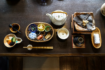 Japanese ryokan breakfast appetizer dishes including  mentaiko, pickle, seaweed, bamboo shoot, hot plate, other side dishes,  green tea pot, cup and warm towel on wooden table