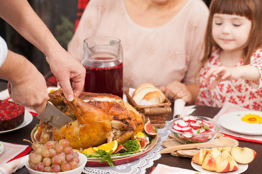 A man cuts off a piece of roast Turkey at the table