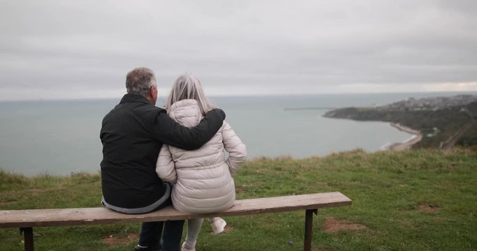 Senior couple sitting on a bench looking at sea view