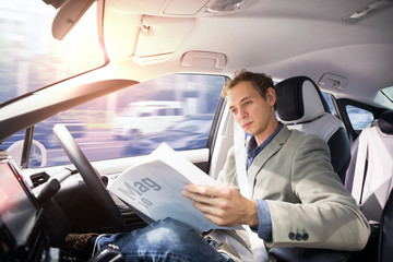 Caucasian driver reading magazine in autonomous car. Self driving vehicle. Driverless car.