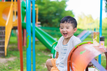 Young Asian boy play a iron train swinging at the playground under the sunlight in summer.