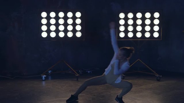 a young professional dancer rehearsing the number on stage in the light of the spotlights. woman in training clothes for warming up muscles. 4k