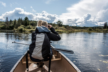 Girl using binocular on Canoe lake of two rivers in the algonquin national park in Ontario Canada on sunny cloudy day