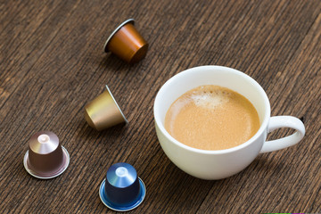 A cup of espresso coffee with colorful aluminium coffee capsules on the wooden table.