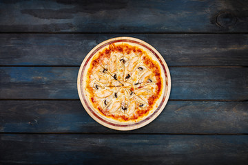Delicious pizza with mushrooms and chicken on a wooden stand on a dark wooden background. Top view center orientation