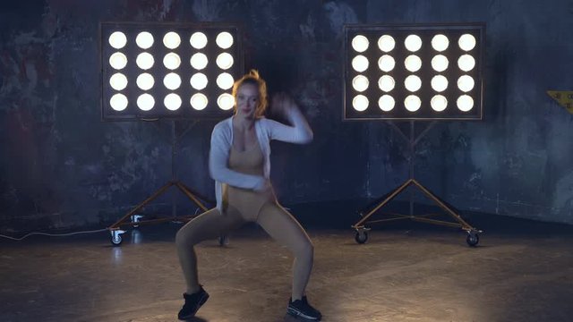 a young professional dancer rehearsing the number on stage in the light of the spotlights. woman in training clothes for warming up muscles. 4k