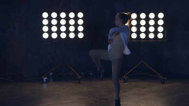 a young professional dancer rehearsing the number on stage in the light of the spotlights. woman in training clothes for warming up muscles. 4k