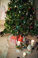 Many lit candles stand on the table on the background of the New Year tree. Background for your text.  Many gifts under the New Year tree. Set of multi-colored gifts