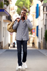 Fototapeta premium Full length young african male traveler walking outdoors and talking cell phone