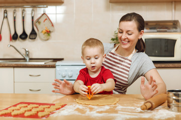 Little kid boy helps mother to cook Christmas ginger biscuit in light kitchen. Happy family mom 30-35 years and child 2-3 roll out dough and cut out cookies at home. Relationship and love concept