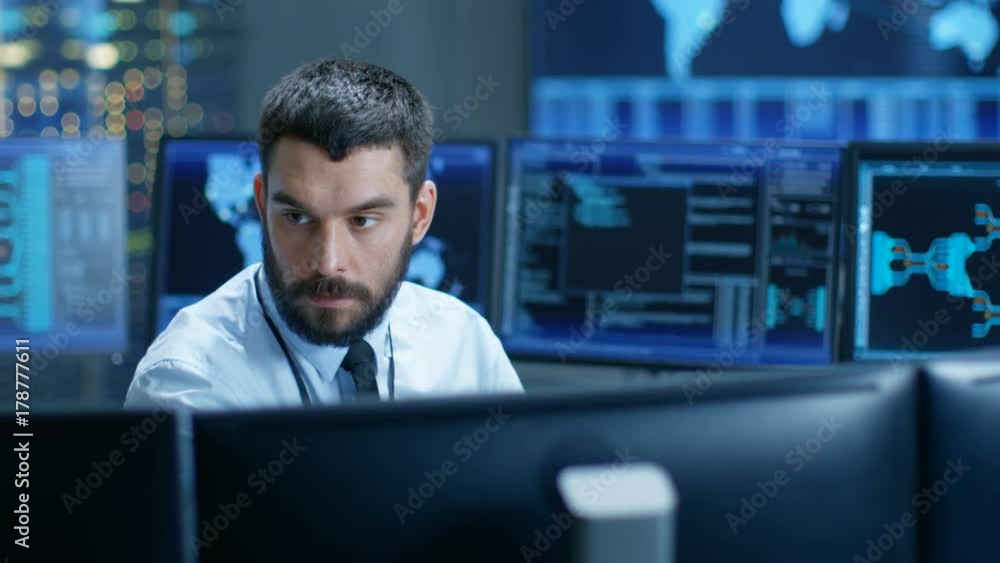 Poster In the Monitoring Room Technical Operator Attentively Monitors Stability of the System. He's Surrounded By Screens Showing Technical Data. Shot on RED EPIC-W 8K Helium Cinema Camera.