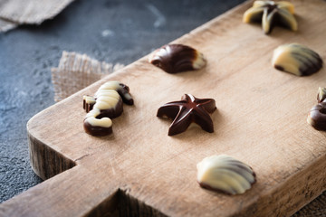 Various raw chocolate candies on wooden board, dark background. Healthy sweets with marine theme
