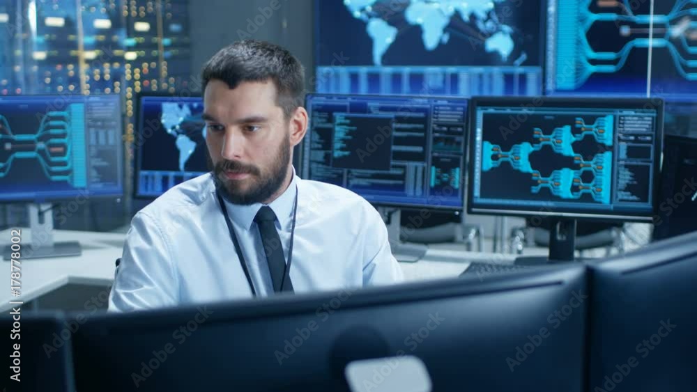 Fototapete In the System Control Center Technical Operator Monitors Displays at His Workstation. He's Surrounded by Displays Showing Relevant Data. In the Background Data with Interactive Map.