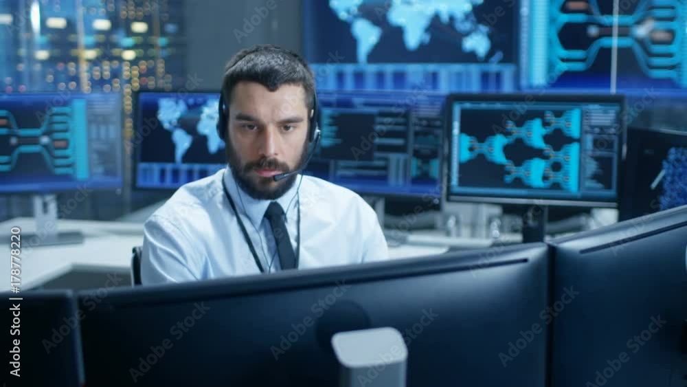 Poster In the System Monitoring Room Dispatcher Wearing Headset Observers Proper Functioning of the Facility. He's Surrounded by Screen Showing Technical Data. Shot on RED EPIC-W 8K Helium Cinema Camera.