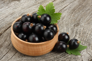 black currant in wooden bowl with green leaf on old wooden background