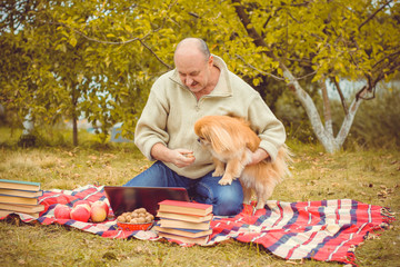 Mature american men wear in sweater sit at picnic with his pet dog. Senior enjoy autumn time at...