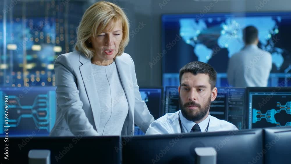 Poster In the System Monitoring Room Head of the Department Controls Work of the Operator. In the Background People Working and Monitors Showing Relevant Technical Data. 