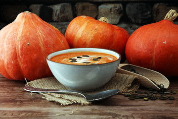 Roasted pumpkin and carrot soup with cream and pumpkin seeds on wooden background