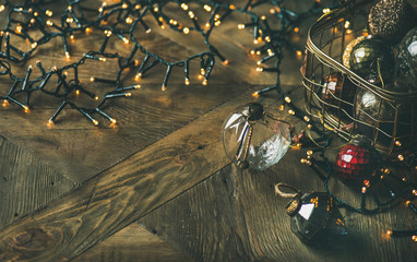 Christmas or New Year background, preparing for holiday. Christmas tree toy decoration glass balls in vintage box and light garland over rustic wooden background, copy space