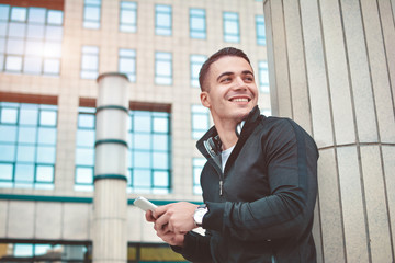 Young casual man using a smart phone texting messages in the street