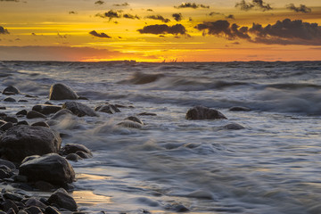 sunset over the sea during the storm, waves crashing against the stones