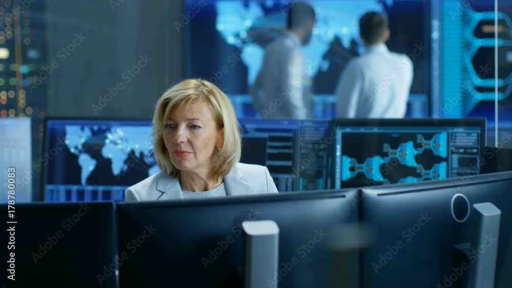 Poster System Monitoring Room Professional Female Operator Observes Correct Functioning of the Facility. In the Background People Working with Interactive Map. Shot on RED EPIC-W 8K Helium Cinema Camera.