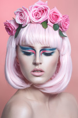 Fashion beauty portrait of a beautiful girl with pink hair, creative make-up and a wreath of roses on her head.