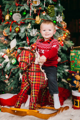Funny little boy plays before green Christmas tree in the room