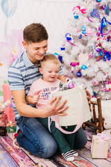 Dad plays with little son before pink Christmas tree