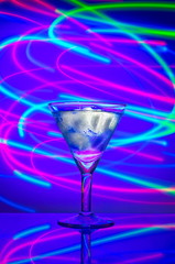 Glass with a cocktail with ice against a background of abstract illumination of colored neon