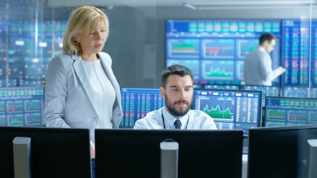 In the Stock Market Firm Chief Executive Talks with Professional Trader. They're Surrounded by Screens with Graphs and Ticker Numbers. Shot on RED EPIC-W 8K Helium Cinema Camera.