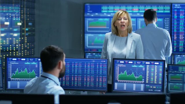 In the Stock Market Selling/ Buying Department Female Manager Talks with Male Trader. In the Background People Working, Screens Show Ticker Numbers and Graphs. 