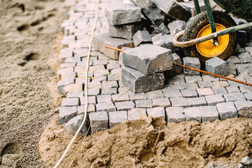 Construction site - details of pavement road building with cobblestone blocks, wheelbarrow and...