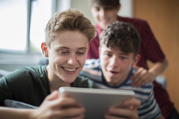 Three Teenage Boys Playing Game On Digital Tablet At Home