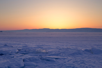 Fototapeta na wymiar Transparent ice floe on a hummock field on the frozen Siberian Lake Baikal at sunset in winter.