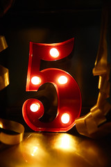 red number five with small bulbs behind the background of a gold metal and on the sides a golden ribbons