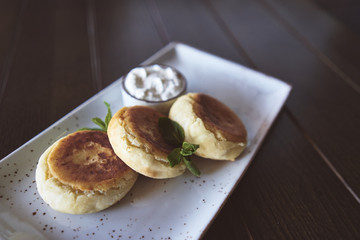 Curd cheese cakes. Greenery. Sour cream. A cafe. Dish. Wooden table. Breakfast
