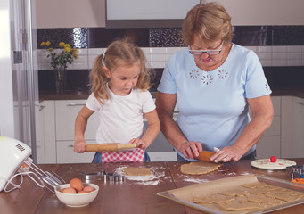 little girl and grandmother roll out the dough