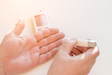 Medicine, diabetes, glycemia, health care and people concept - Close up of man hands using lancet on finger to check high blood sugar level with glucometer or glucose meter at home