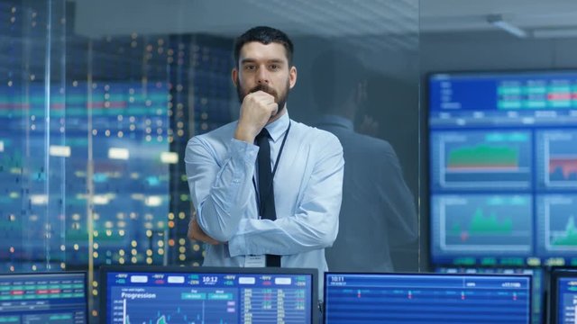 Stock Market Top Trader Thinking Hard on Selling Stocks at the Best Time. Behind Him People Working and Monitors Show Graphs and Ticker Numbers. Shot on RED EPIC-W 8K Helium Cinema Camera.