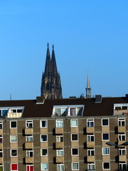 Altes Mietshaus in Braun mit Balkons in Beige vor blauem Himmel im Sonnenschein mit dem Kölner Dom...