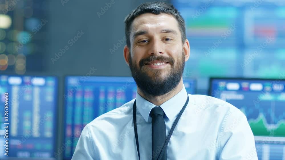 Aufkleber Handsome Stock Market Trader Thinks and Smiles into the Camera. Behind Him Computer Monitors Showing Ticker Numbers and Graphs. Shot on RED EPIC-W 8K Helium Cinema Camera.