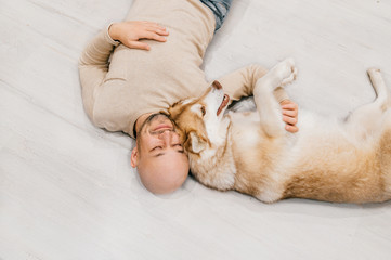 Adult bald man with husky puppy sleeping on floor. Owner with pet together at home. Kind and soulful emotions. Lovely dog resting with young male. Guy with beloved domestic animal hugging each other.